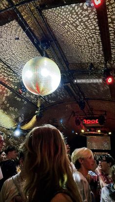 a group of people standing in a room with lights on the ceiling and disco balls hanging from the ceiling