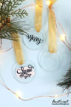 three christmas ornaments hanging from a tree with gold ribbon and lights around them on a white surface