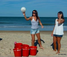 two women on the beach playing frisbee with buckets in front of them