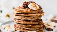 a stack of pancakes topped with bananas and pecans