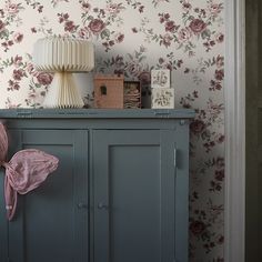 a blue cabinet sitting next to a wall covered in pink and purple flowers with a lamp on top