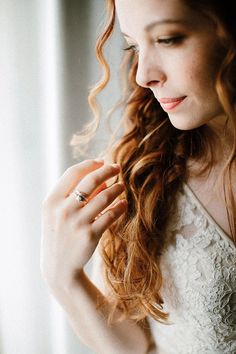 a woman with long red hair wearing a wedding dress and holding a ring on her finger