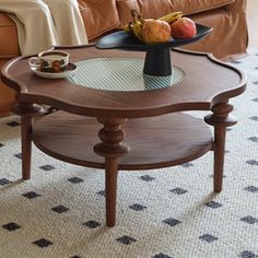 a coffee table with fruit on it in front of a brown couch and white rug