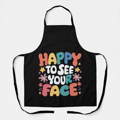 a black apron with the words happy to see your face on it and colorful flowers