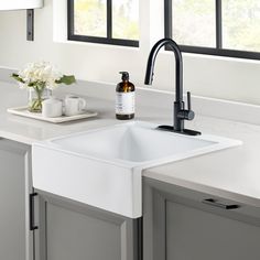 a white kitchen sink sitting under a window next to a vase with flowers on it