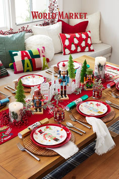 the table is set for christmas dinner with red and white plates, silverware, napkins, candles and other holiday decorations