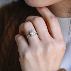 a close up of a person wearing a ring with a princess cut diamond on it