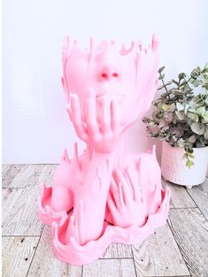 a pink sculpture sitting on top of a wooden floor next to a potted plant