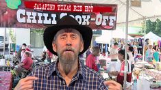 a man wearing a hat standing in front of a tent with chili cook - off signs on it