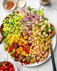 a large salad on a white plate topped with tomatoes, lettuce and chickpeas