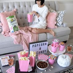 a woman sitting on a couch with popcorn and candy in front of her holding a pink bag