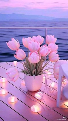 pink tulips are in a white vase on a wooden table near the water