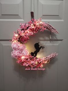 a wreath with pink flowers and a silhouette of a girl on it hanging from the side of a door