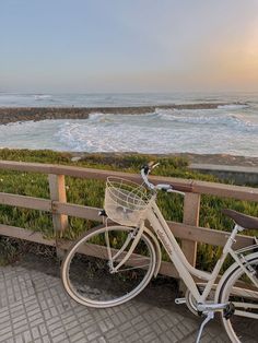 a white bicycle parked next to a wooden fence near the ocean with waves in the background