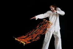 a man with long hair and white clothes is holding beads in his hand while standing against a black background