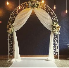 a wedding arch decorated with flowers and white draping for the entrance to the ceremony