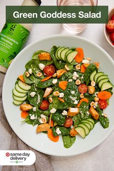 a white plate topped with cucumbers, carrots and spinach next to a bottle of green goddess salad