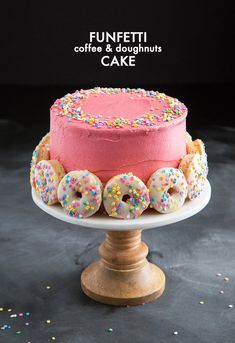 a pink frosted cake with sprinkles and donuts on the top