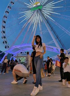 a woman standing in front of a ferris wheel at night with other people around her