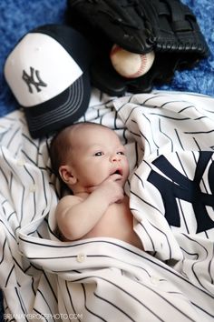 a baby laying on top of a baseball uniform next to a hat and glove,