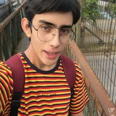 a young man with glasses and a striped shirt is standing on a bridge looking at the camera