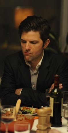 a man sitting at a table with food and wine in front of him, looking down