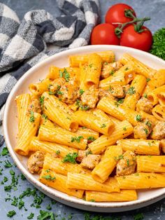 a white bowl filled with pasta and meat on top of a table next to tomatoes