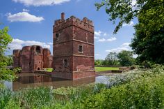 an old brick building sitting on top of a lush green field next to a river