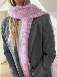 a woman wearing a pink knitted scarf and grey blazer standing in front of a white wall