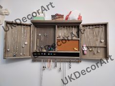 a jewelry cabinet with many necklaces hanging from it's sides and two shelves on the wall