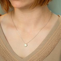 a woman wearing a necklace with a pearl on it