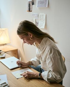 a woman sitting at a desk writing on a piece of paper with a pen in her hand