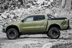 a pick up truck with graffiti on the side driving down a dirt road next to rocks