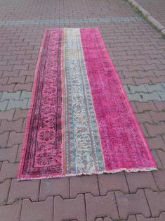 a pink and blue rug laying on the ground in front of a brick sidewalk with cobblestones