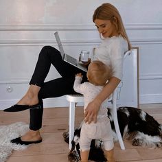 a woman sitting on a chair holding a baby and looking at a laptop computer screen