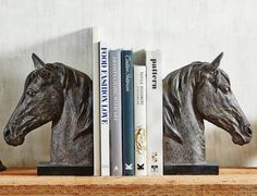 two horse head bookends sitting on top of a wooden shelf next to books