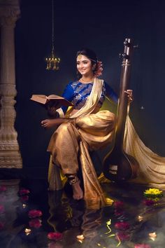 a woman sitting on top of a wooden floor holding a book and wearing a sari