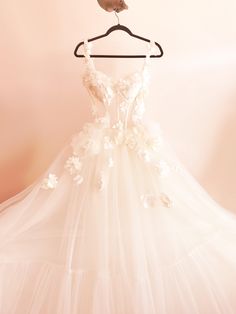 a wedding dress hanging on a hanger in front of a pink wall with a bird perched on it