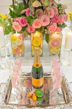 a bottle of champagne sitting on top of a silver tray next to candles and flowers