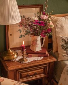 a table with flowers and a candle on it next to a bed in a room