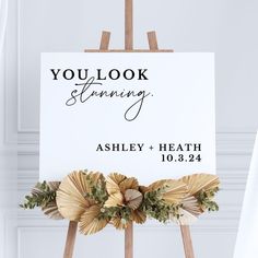 an easel holding a sign that says you look stunning with flowers and leaves on it