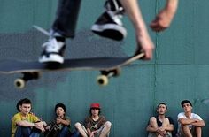 a skateboarder doing a trick in front of a group of young men sitting on the ground