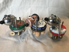 three small tea kettles with handles and knobs on wheels, one has a spoon in it