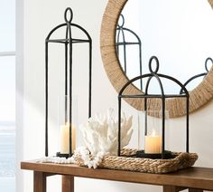 two candles on a table next to a mirror and basket with seashells in it