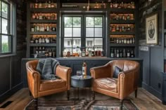 two leather chairs sitting next to each other in front of a bar with bottles on the shelves