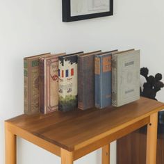 a wooden table topped with three books next to a framed picture on the wall above it