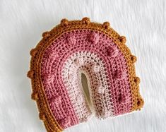 a crocheted pink and brown object laying on top of a white blanket with a hole in the middle