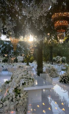 an outdoor wedding setup with white flowers and chandeliers hanging from the trees in the background