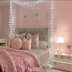 a bedroom decorated in pink and white with lights on the ceiling, bedding and pillows