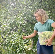 a woman holding a bucket full of green apples